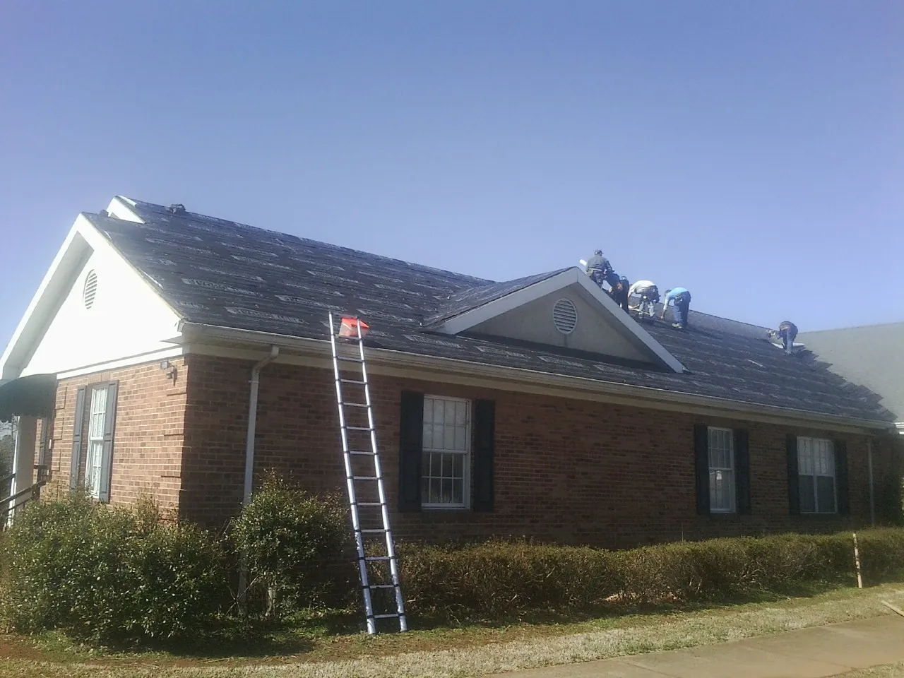 Crew tearing shingles off a brick ranch roof with a ladder set — Metal Roof Repair work by our crew in Wyandanch