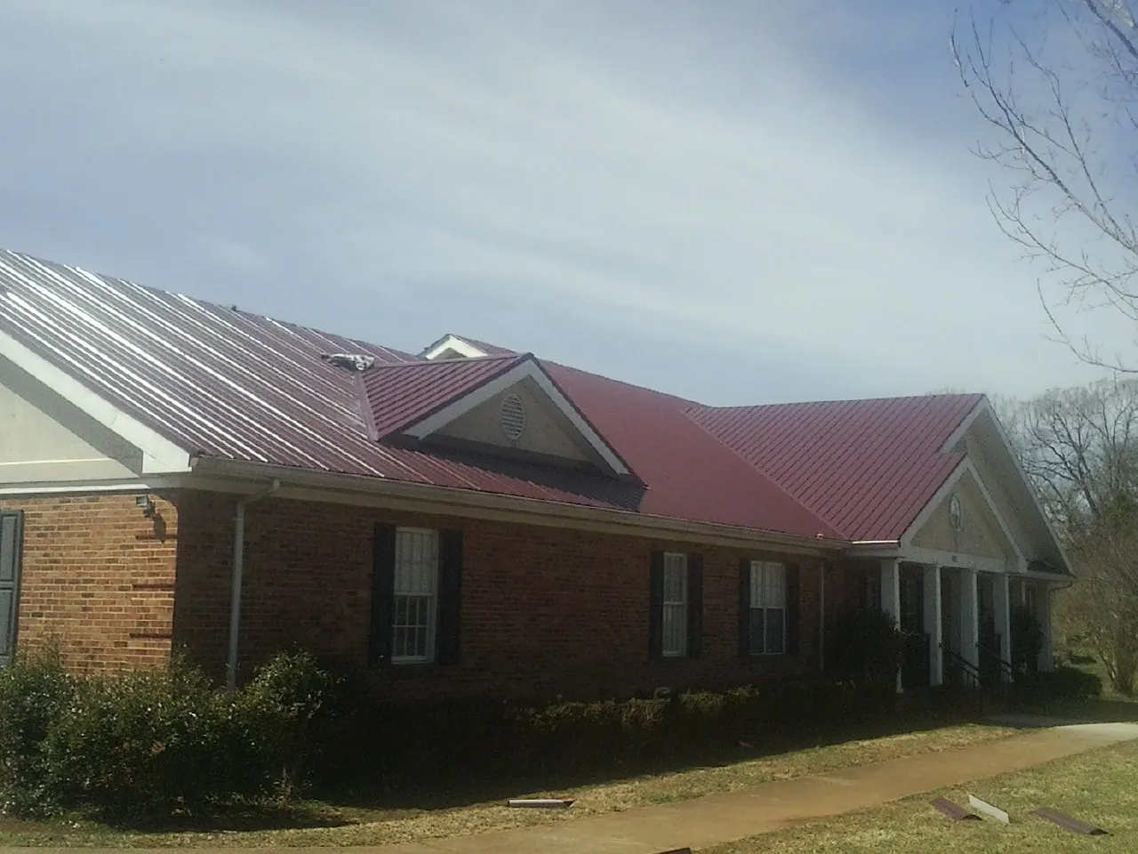 Red metal roof with gabled entries on a long brick building, from a Hail Damage Roof Repair job in Wyandanch