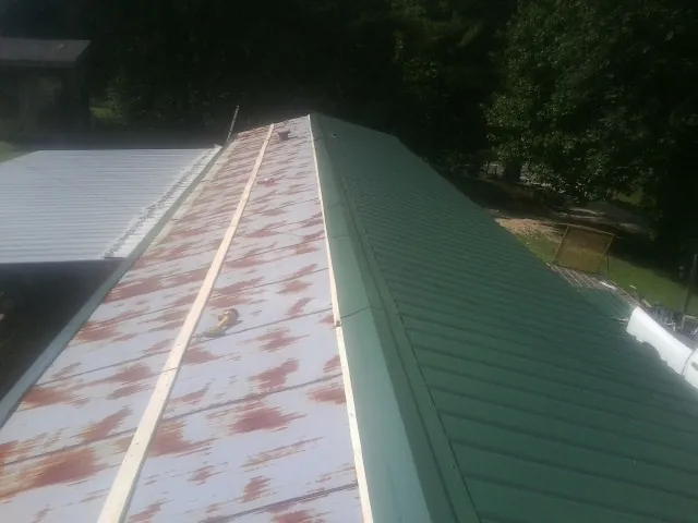 Old rusted panels beside newly installed green metal roofing — Wind Damage Roof Repair by Roofing Brothers in Wyandanch
