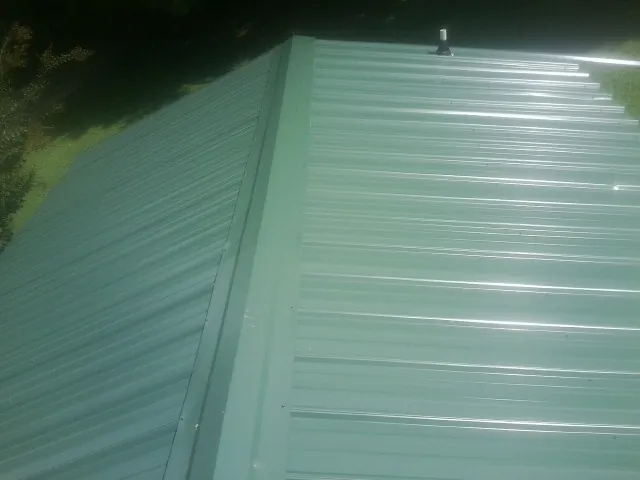 New green metal panels meeting at the ridge of a roof — Flat Roof Repair work by our crew in Wyandanch