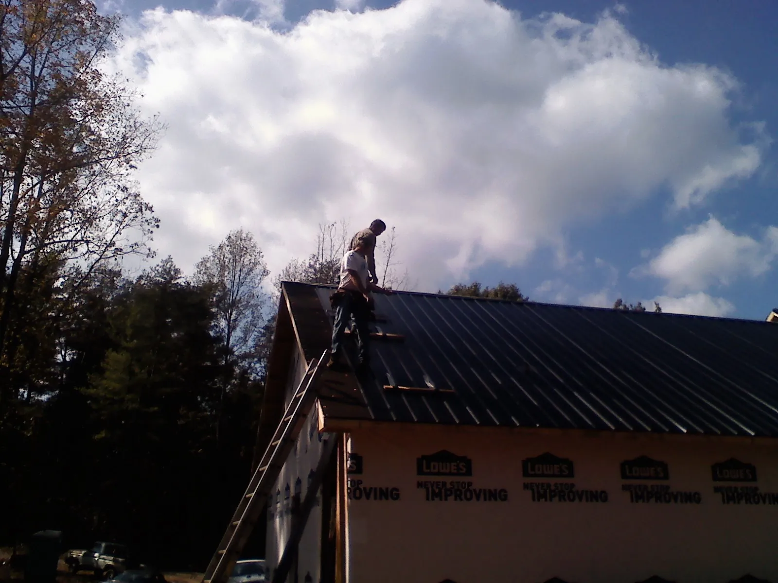 Roofer fastening dark metal panels high against a cloudy sky, from a Roof Inspection job in Wyandanch