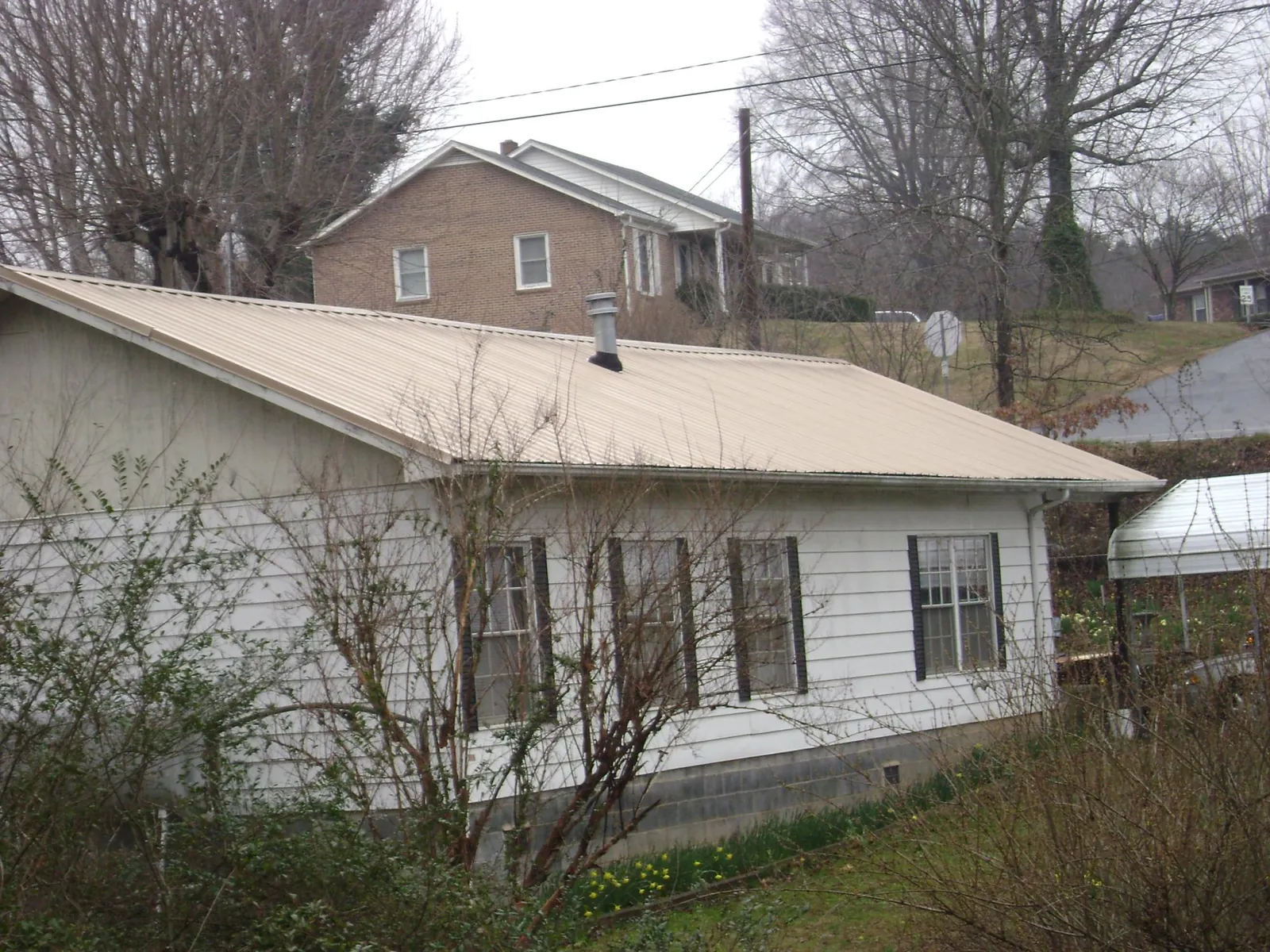 Tan metal roof on a white sided house set into a hillside — Commercial Roofing by Roofing Brothers in Wyandanch